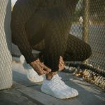 a man tying his white tennis shoes on the sidewalk