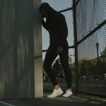 a man in a black hoodie leaning against a fence