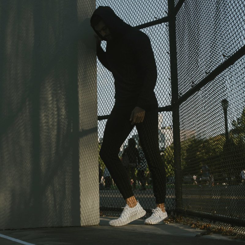 a man in a black hoodie leaning against a fence